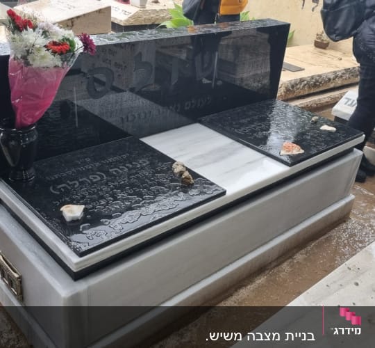 מצבה שחורה עם כיתוב ופרחים באגרטל